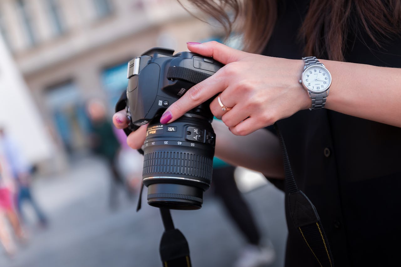 services-04 A woman adjusting a DSLR camera outdoors, focusing on her hands and device. Perfect for photography themes.