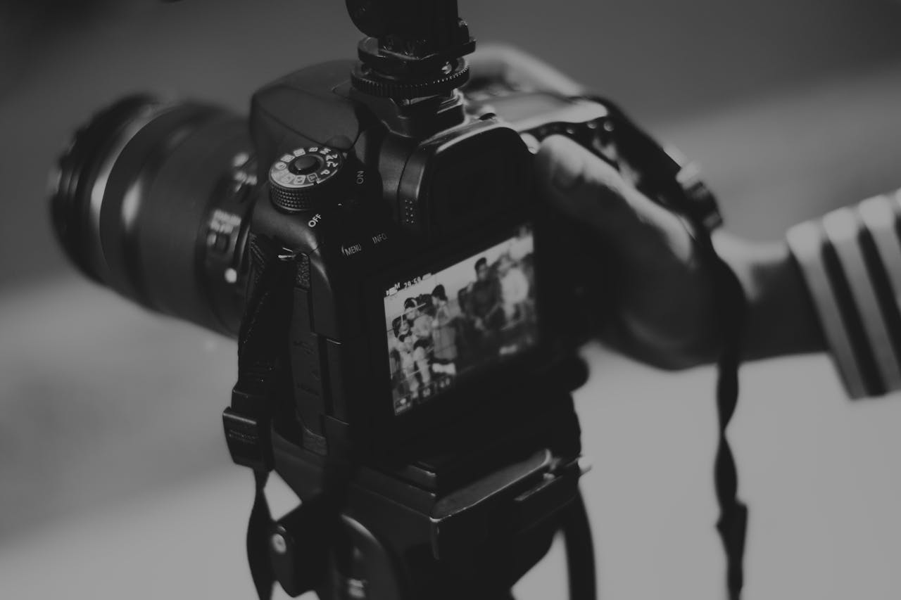 services-01 Black and white image of a DSLR camera capturing people in focus, showcasing photography professionalism.