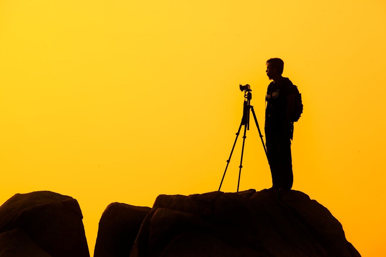 services-02 Silhouette of a lone photographer with tripod on a rocky cliff against a golden sunset sky.